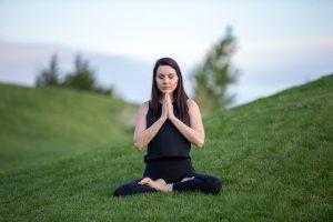 Woman wearing black clothes meditating in the middle of a green field